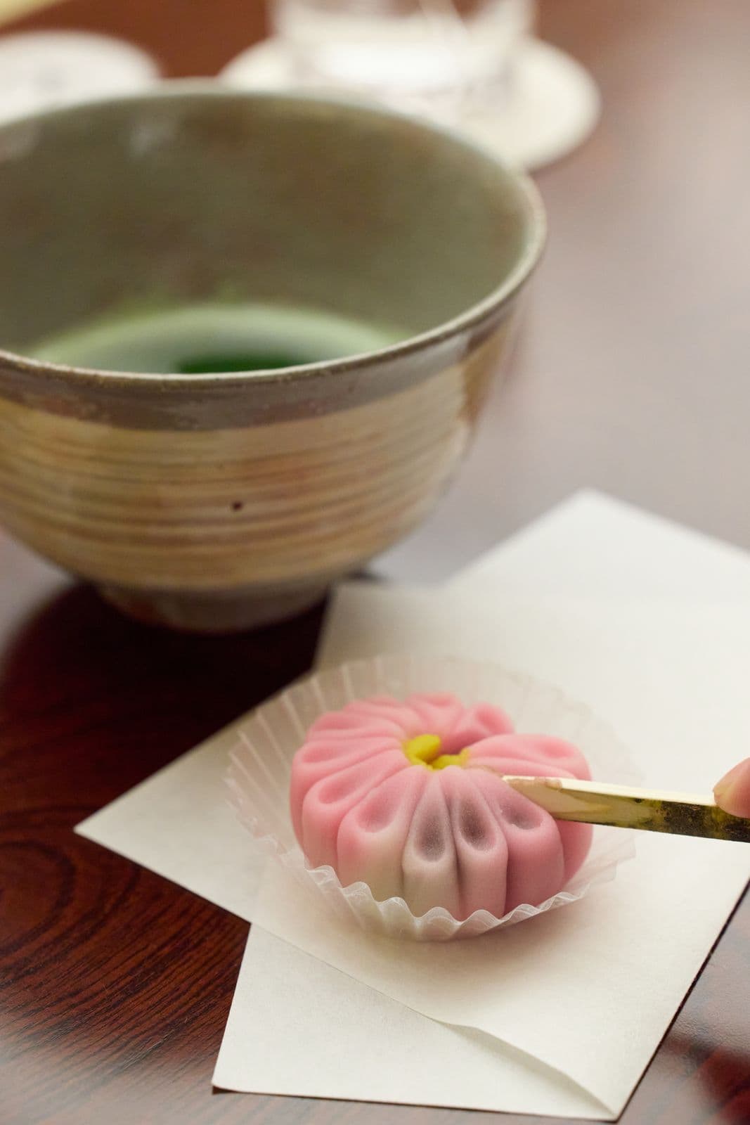 白色和紙上的粉紅色菊花造型和菓子,後方是一碗抹茶。