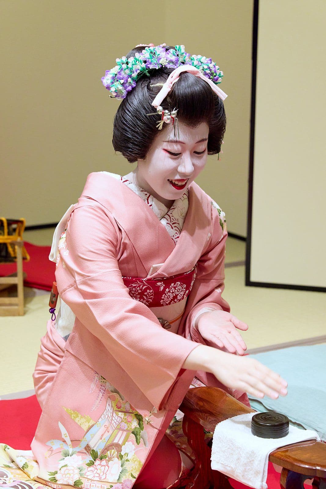 在「金毘羅船船」中,一位穿粉紅色和服的藝妓伸手去拿放在扶手上的小蓋子「袴」(hakama)。