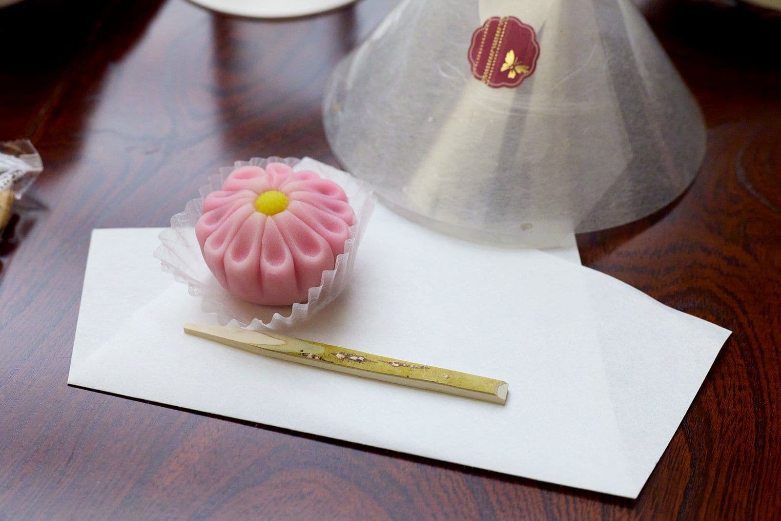 白紙上一個粉紅色、菊花造型的日式點心。