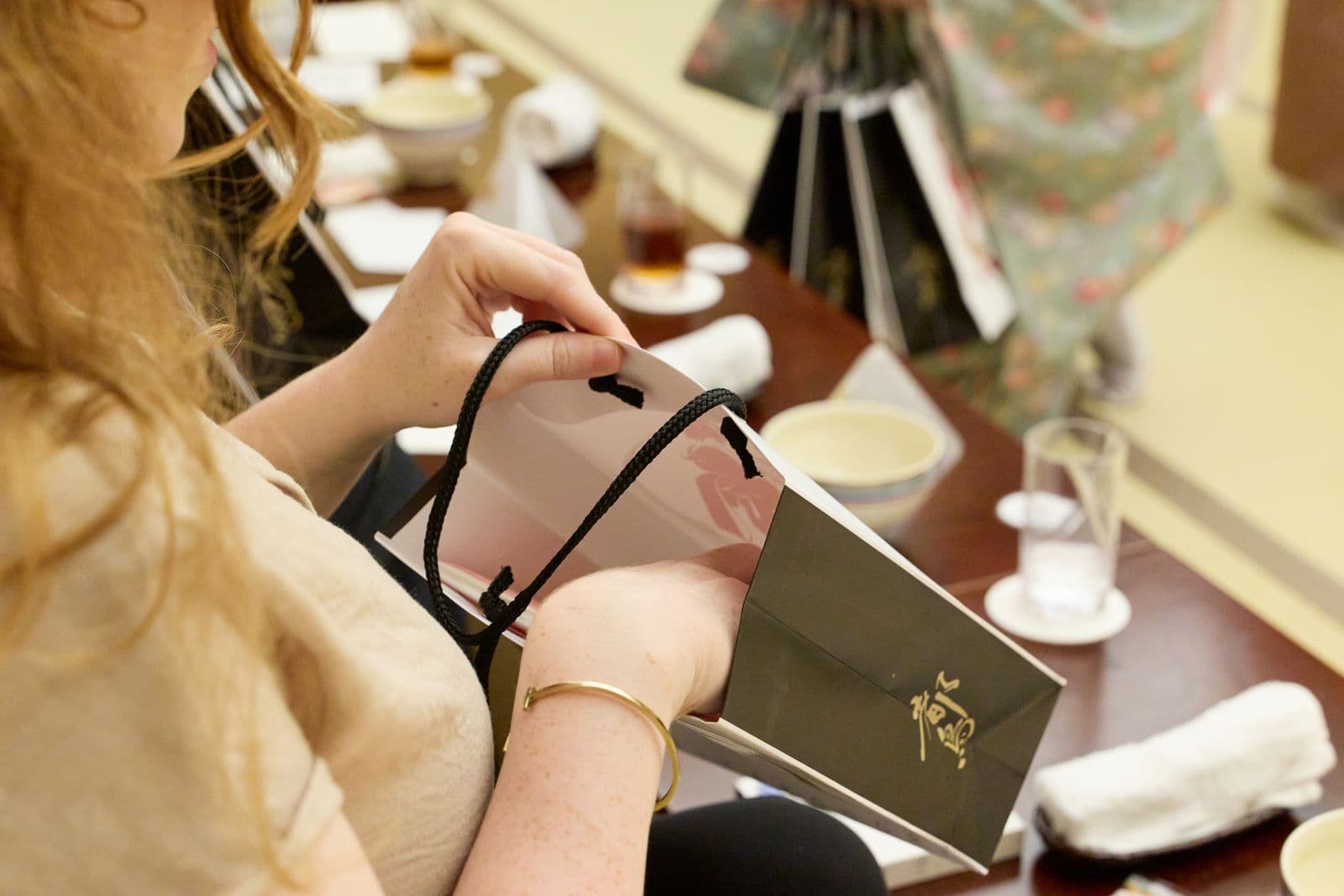 一位賓客在擺著茶杯的桌旁,打開印有金色「Miyakodori」字樣的黑色禮袋。