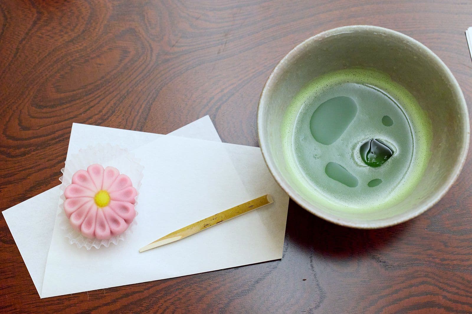 白色紙上,一碗抹茶旁放著粉紅色菊花造型的和菓子。