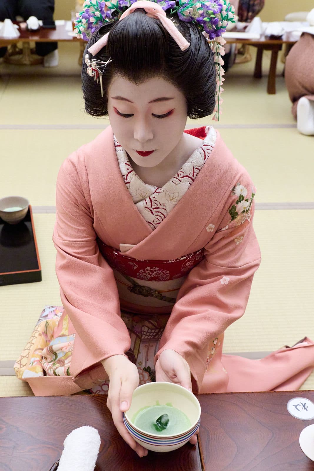 身穿粉紅色和服的藝妓,將一碗抹茶放在矮桌上。
